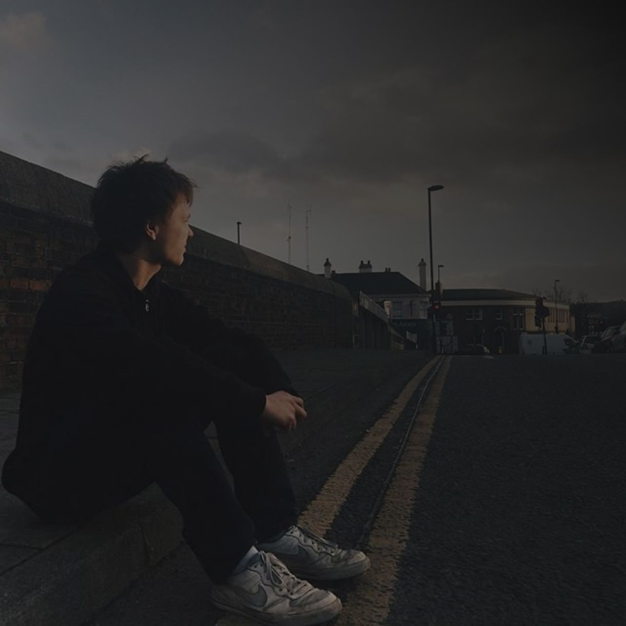 Whitesand sitting on a road curb with a distant look.